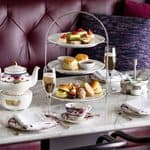 A three-tier Fairmont Empress afternoon tea service featuring finger sandwiches, scones, and small desserts, accompanied by a teapot and glasses of champagne on a marble table.