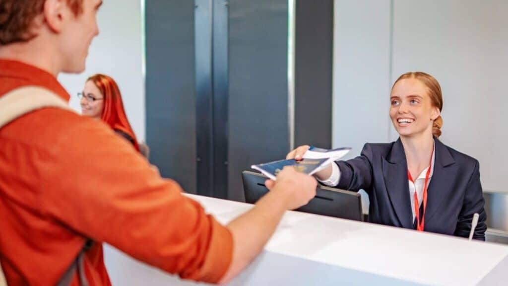 An airline representative at a check-in desk hands a passport, required for a REAL ID domestic flight, to a passenger.