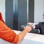 An airline representative at a check-in desk hands a passport, required for a REAL ID domestic flight, to a passenger.