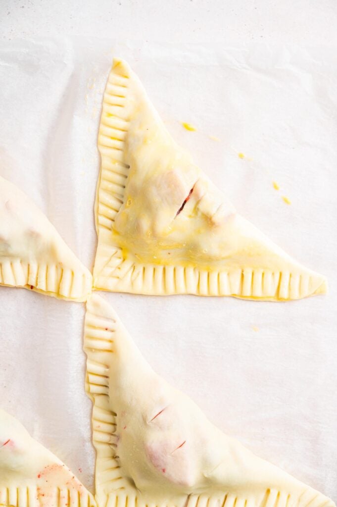 Unbaked triangular fruit turnovers arranged on parchment paper.
