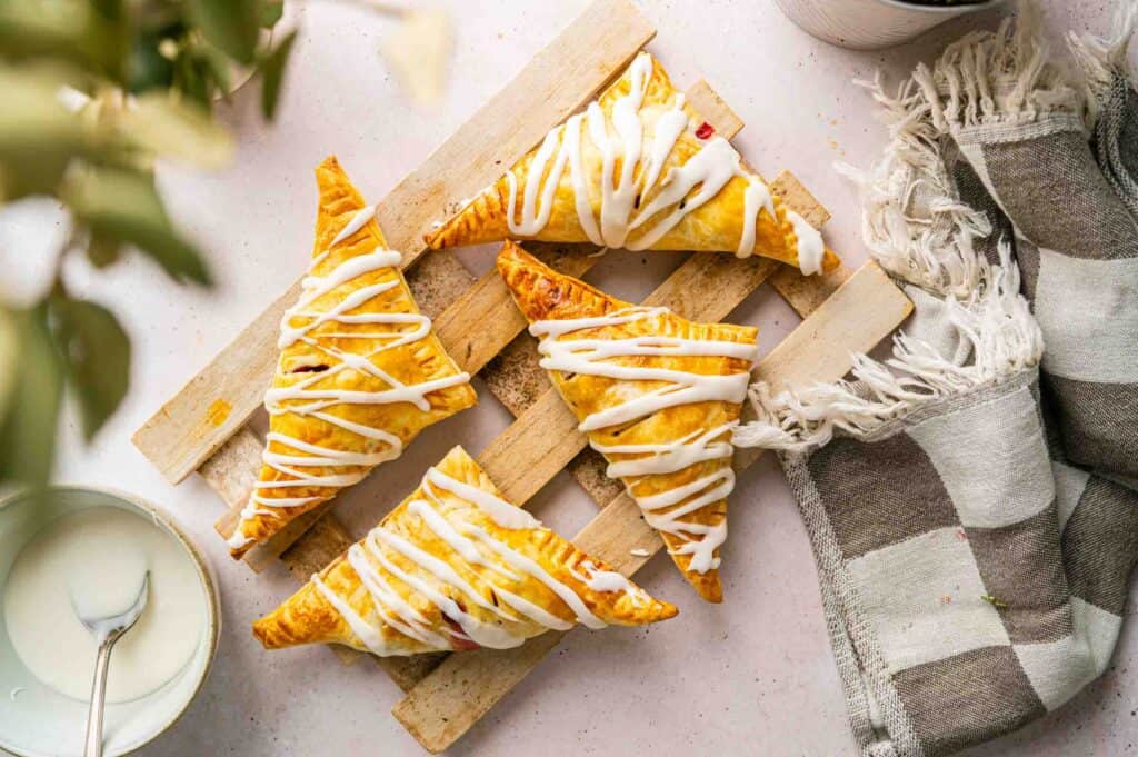 Four triangle-shaped pastries drizzled with white icing on a wooden board.