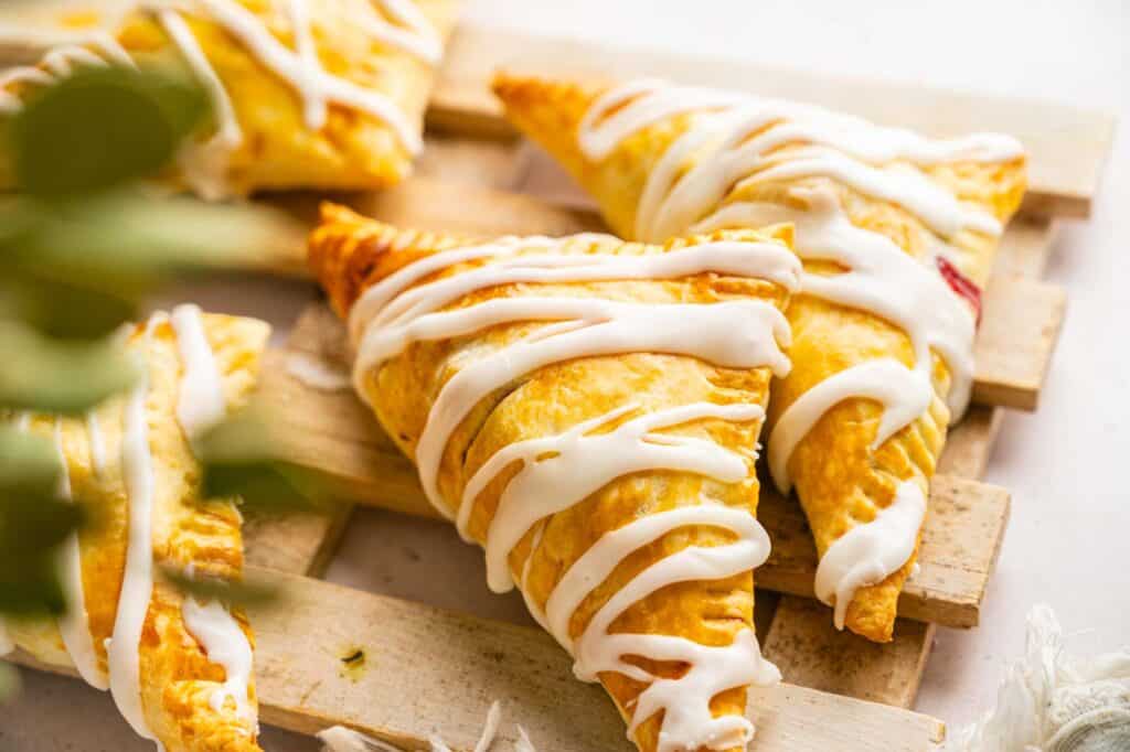 Triangular fruit-filled pastries drizzled with white icing on a wooden board.