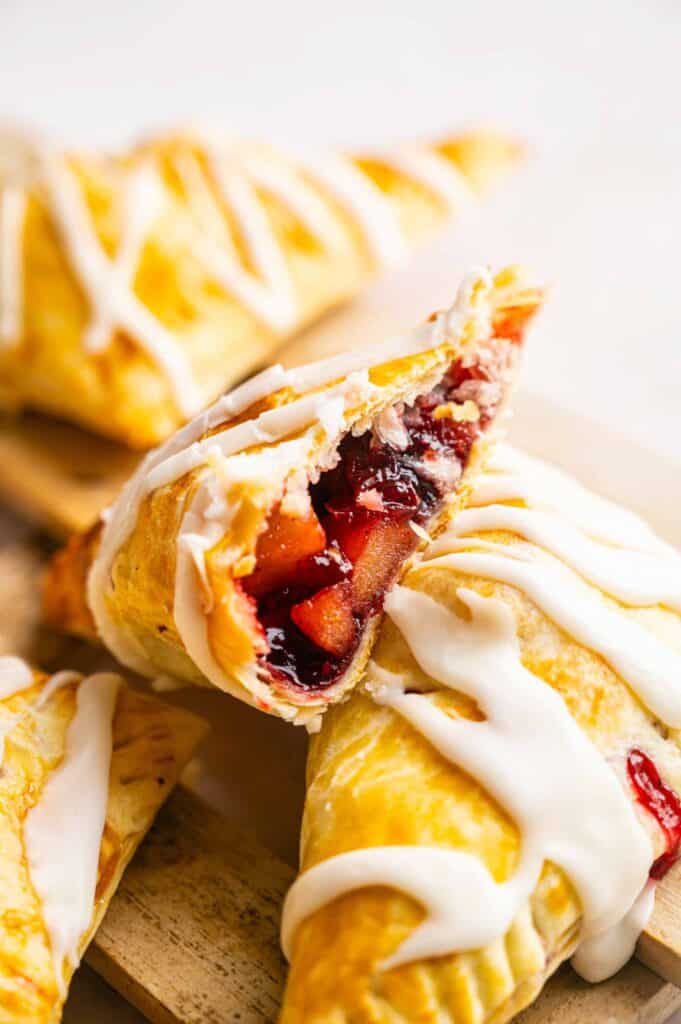Three fruit-filled hand pies drizzled with white icing, one broken open to show the filling.