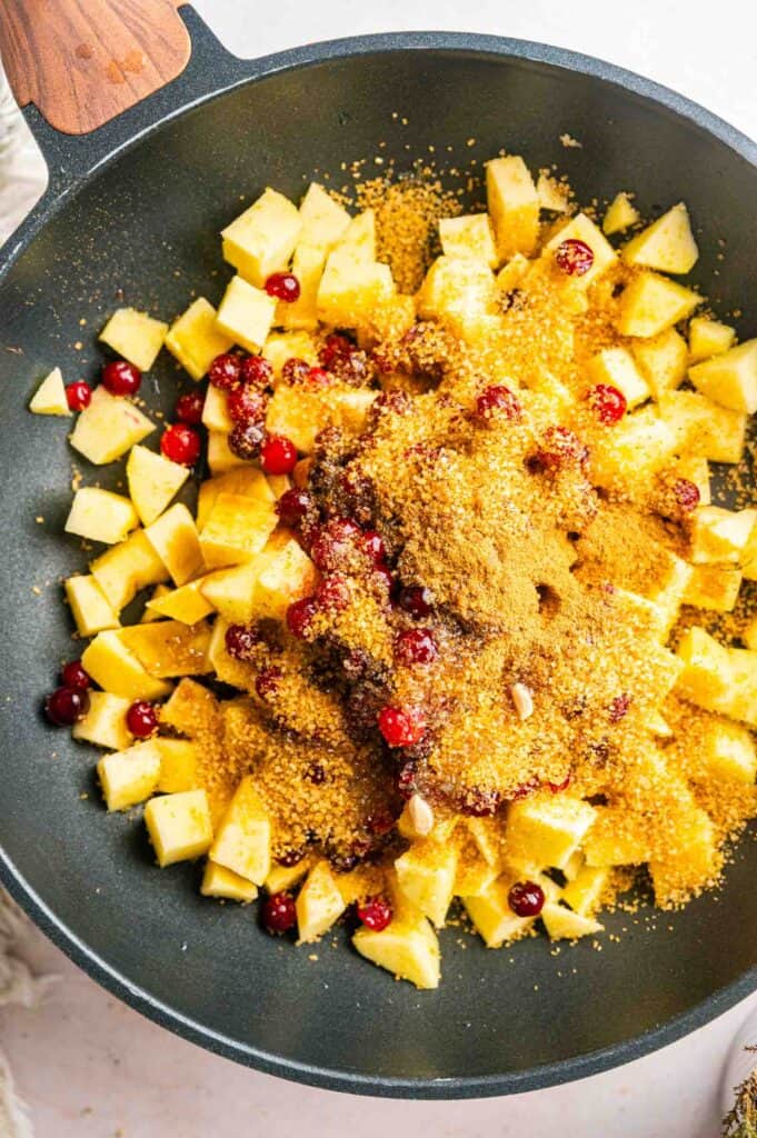 Diced apples and cranberries in a pan topped with brown sugar and spices.