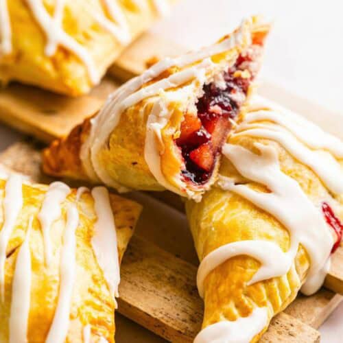 Three fruit-filled pastry turnovers drizzled with white icing, one split open to show a berry filling.