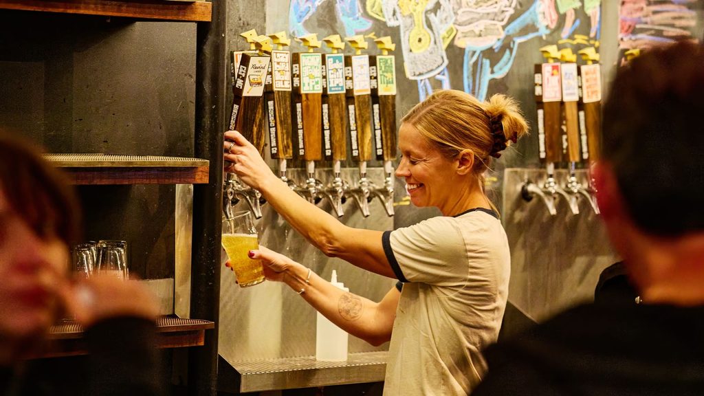 A smiling bartender pours a glass of beer from a tap at a Charlotte brewery.