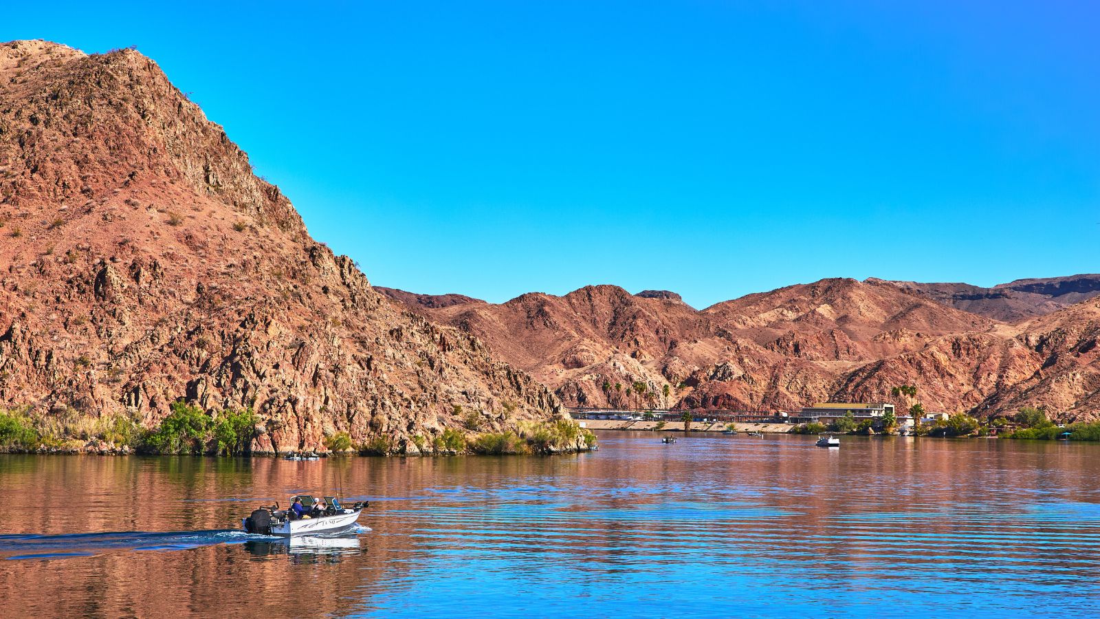 A motorboat travels across a wide river framed by rocky desert mountains.