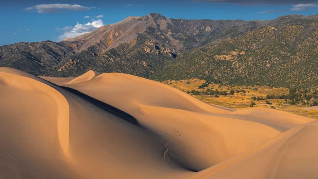 Sand dunes in the foreground set against a mountain range in one of the quiet national parks in fall.