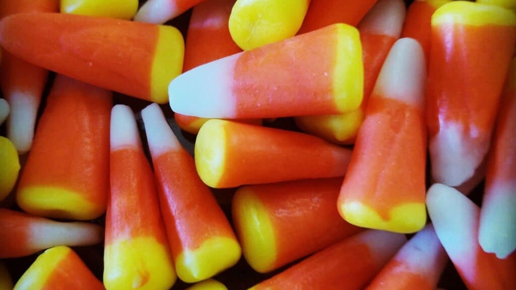 A pile of candy corn pieces, a classic among candy corn treats, each with a yellow base, orange center, and white tip.