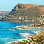 A view of the coastal town of Kalk Bay with a harbor, turquoise water, and a mountain rising in the background.