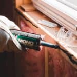A gloved hand applies Mono acoustic sealant to a window frame to weatherproof the home before a cold snap.