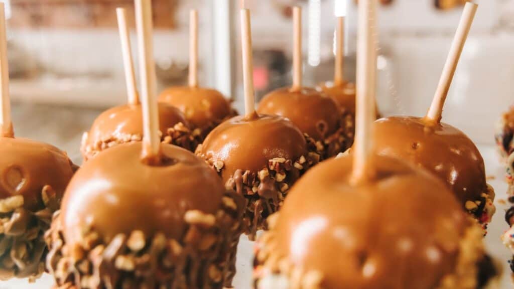 A row of caramel apples with chopped nut toppings on sticks.