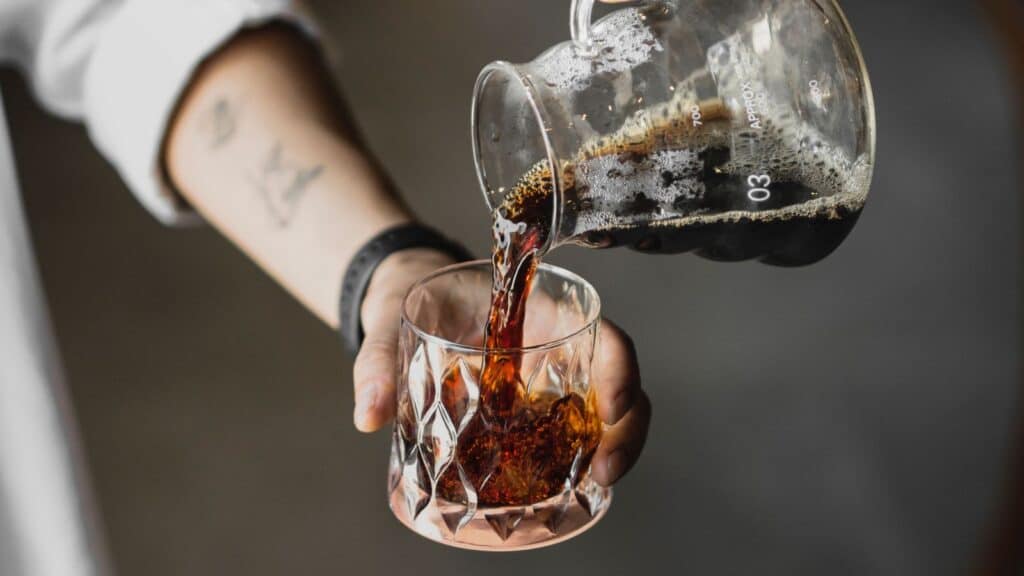 Coffee being poured from a glass carafe into a patterned tumbler, signaling the fall iced to hot coffee switch.