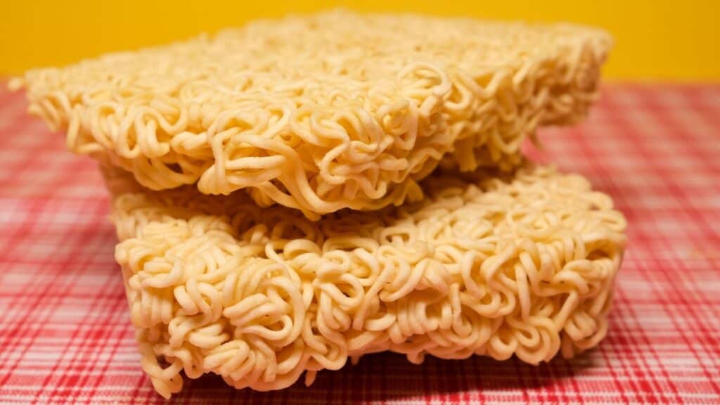 Two dry blocks of college ramen noodles stacked on a red and white checkered surface.