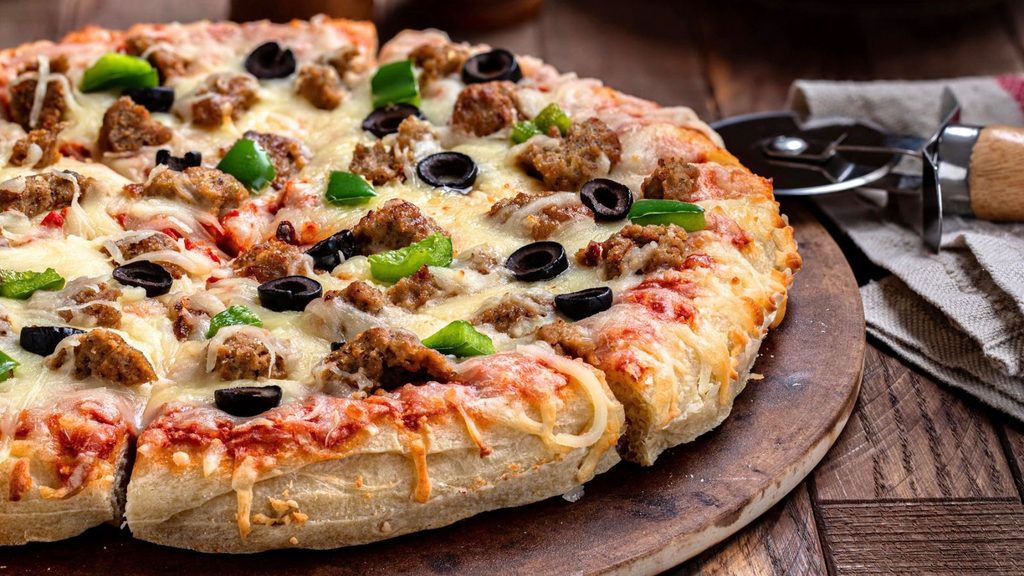 Sausage, green pepper, and black olive pizza on a wooden board with a pizza cutter, perfect for National Sausage Pizza Day.