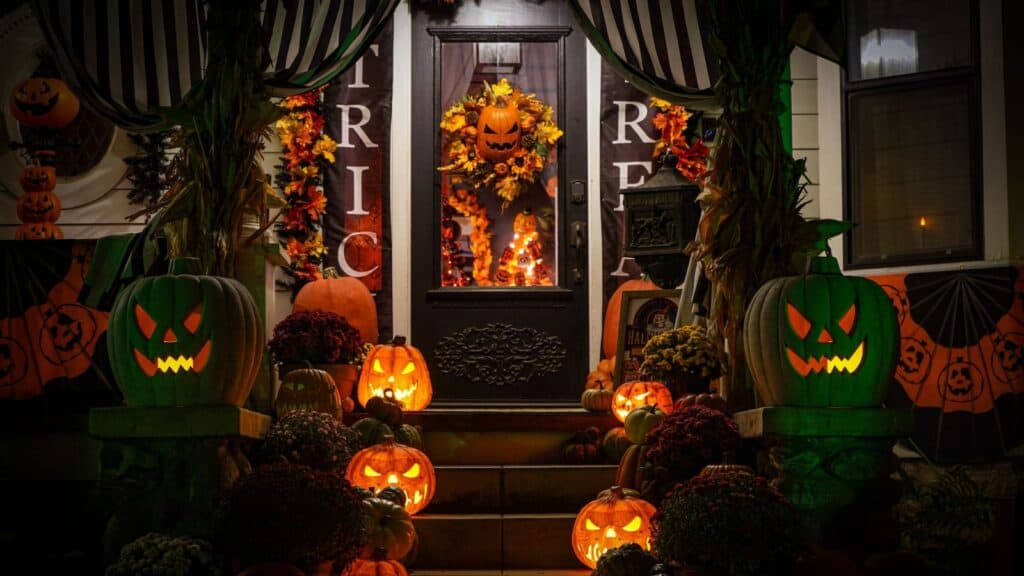 A front porch decorated for Halloween with glowing jack-o&rsquo;-lanterns, autumn foliage, and &ldquo;Trick or Treat&rdquo; banners that comply with HOA Halloween rules.