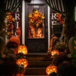 A front porch decorated for Halloween with glowing jack-o’-lanterns, autumn foliage, and “Trick or Treat” banners that comply with HOA Halloween rules.