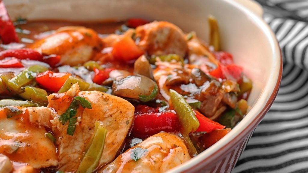 A ceramic dish filled with chicken cacciatore, featuring pieces of chicken, bell peppers, and mushrooms in a red sauce.