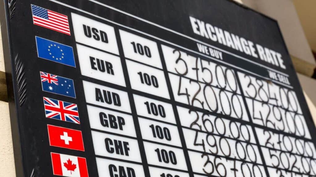 Currency exchange rate board showing flags and buy/sell prices for various international currencies, highlighting common airport currency exchange traps.