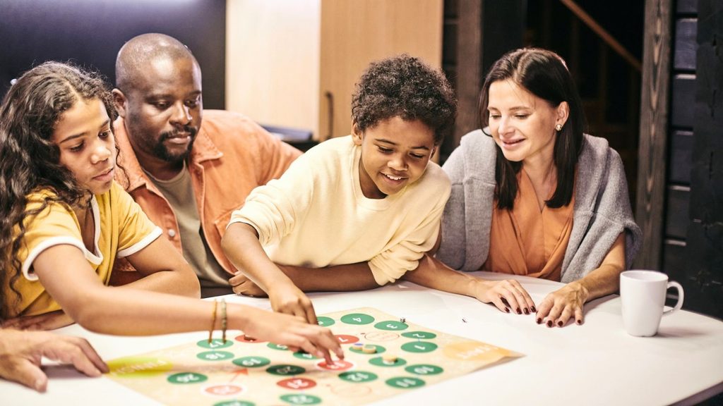 A family of four enjoying a game night while playing a board game at a table.