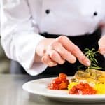 A chef garnishes a plated fish dish with a sprig of rosemary.