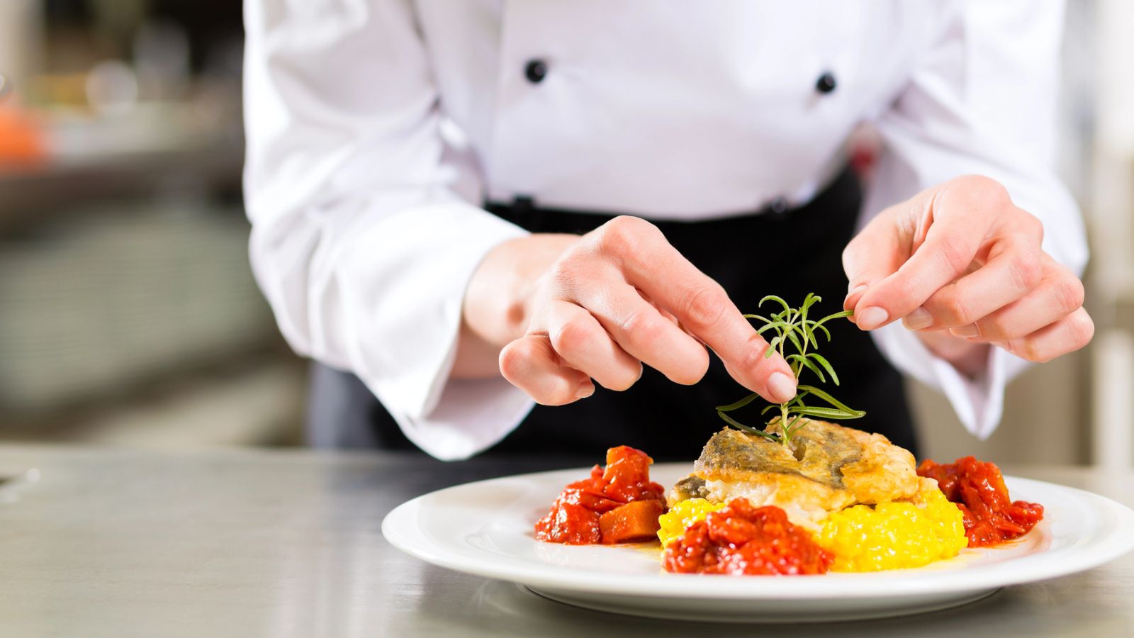 A chef garnishes a plated fish dish with a sprig of rosemary.