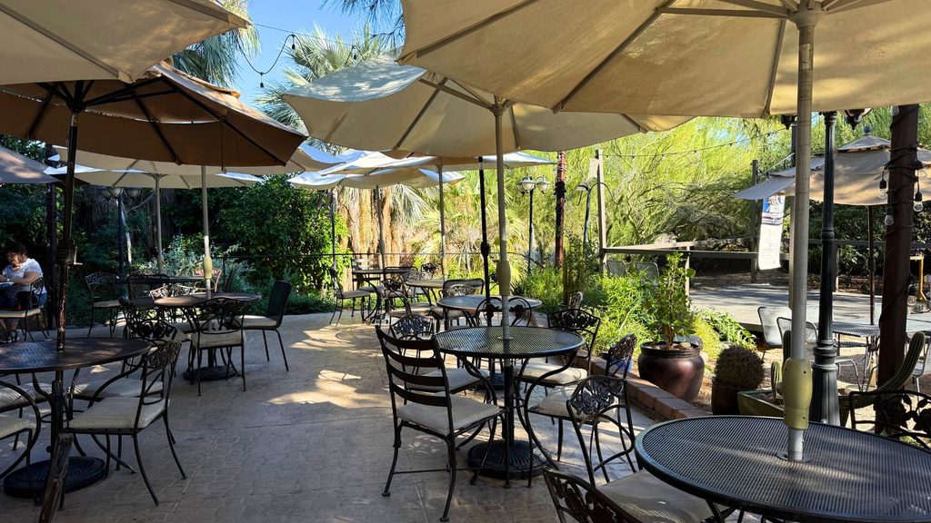 Outdoor patio seating with multiple round tables and chairs arranged under beige umbrellas in Tucson city.