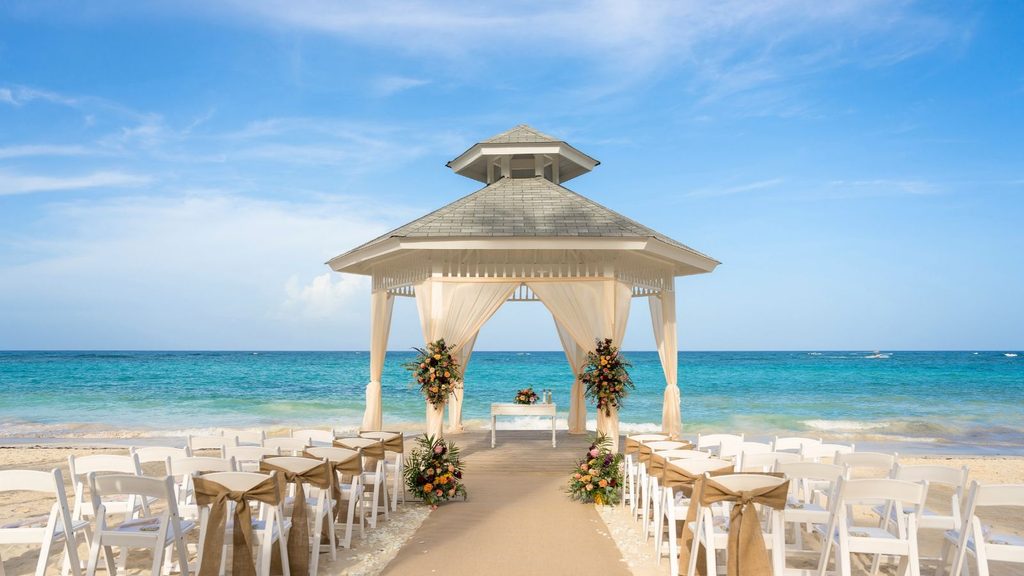 A beach wedding setup with a gazebo, white chairs, and floral arrangements facing the ocean, perfect for Caribbean wedding packages.
