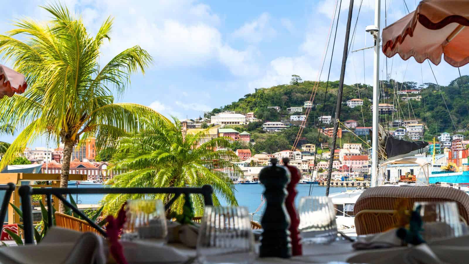 View from a Grenada restaurant patio overlooking a harbor and a hillside city with colorful buildings.