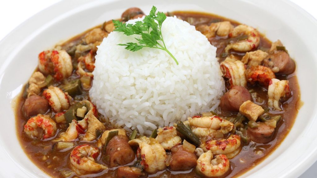 A bowl of gumbo with shrimp and sausage, perfect for National Gumbo Day, served with a scoop of white rice topped with a parsley sprig.