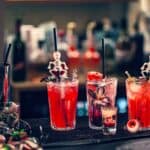 Three Halloween cocktails served in glasses on a bar counter, each decorated with skeleton swizzle sticks and festive garnishes.