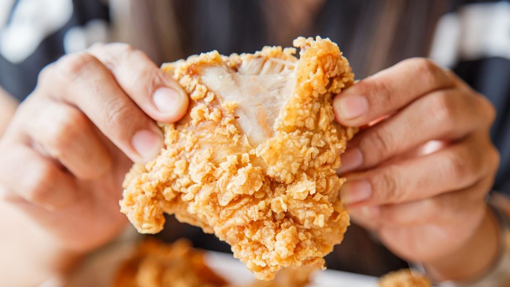 Hands holding a piece of crispy fried chicken to celebrate National Greasy Foods Day.