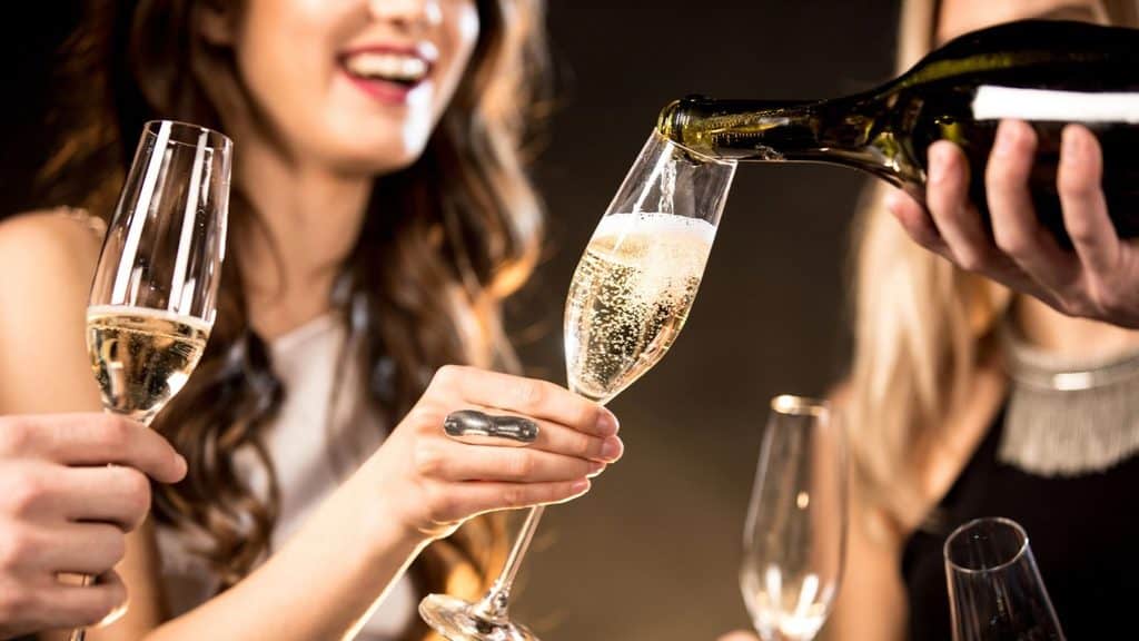 Sparkling wine being poured into a flute held by a woman, with another woman holding a glass nearby.