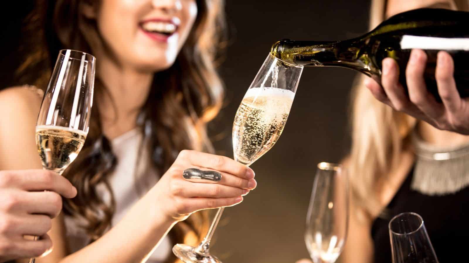 Sparkling wine being poured into a flute held by a woman, with another woman holding a glass nearby.
