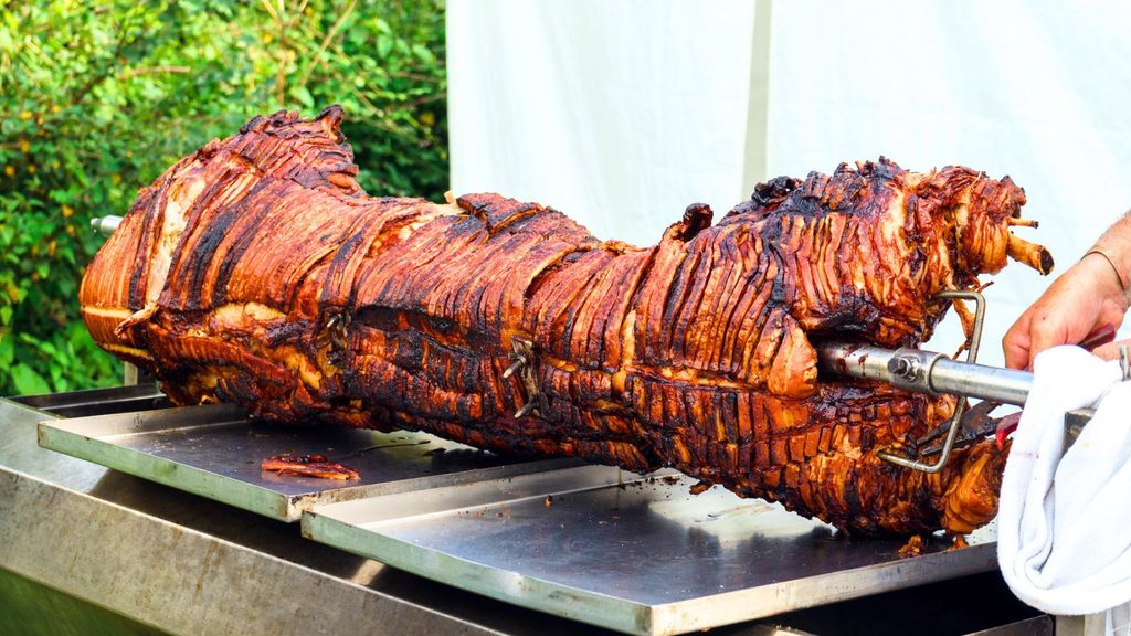A roasted hog on a metal spit over a stainless steel tray.