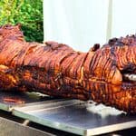 A roasted hog on a metal spit over a stainless steel tray.