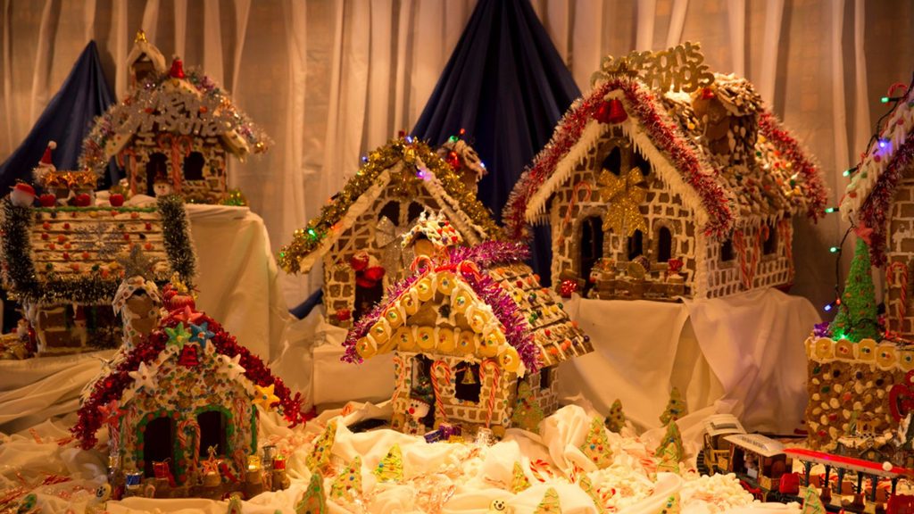 A collection of decorated gingerbread houses arranged on a table with festive trim and lights.