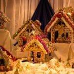 A collection of decorated gingerbread houses arranged on a table with festive trim and lights.