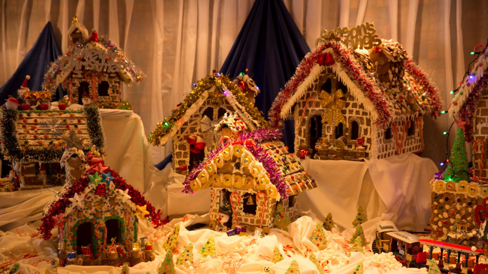 A collection of decorated gingerbread houses arranged on a table with festive trim and lights.