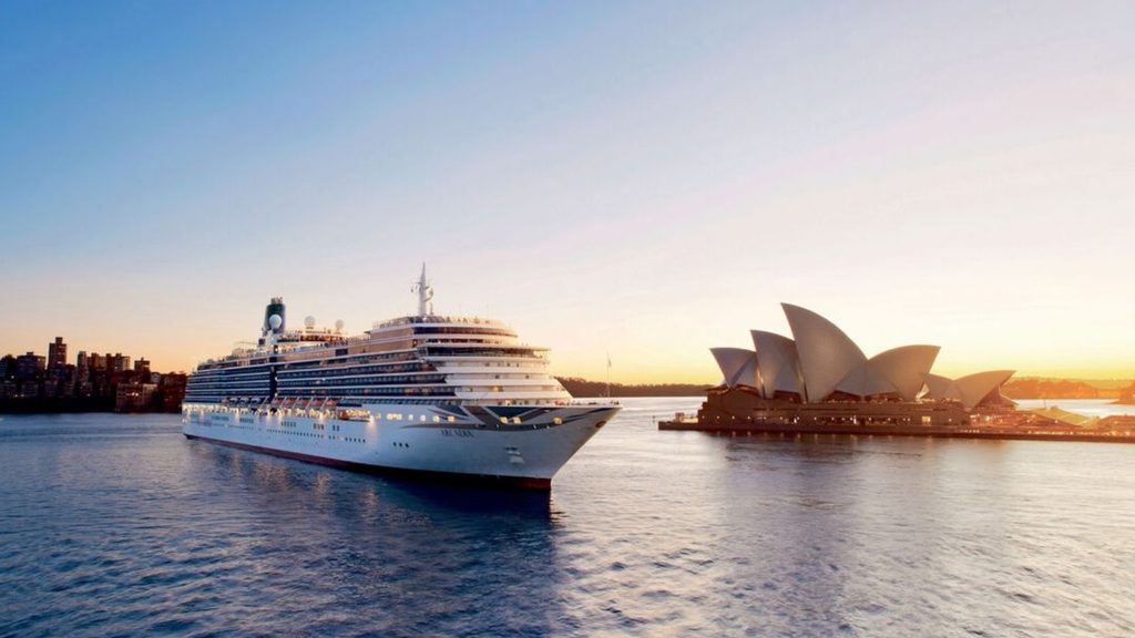 A large cruise ship sailing past the Sydney Opera House at sunrise.