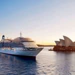 A large cruise ship sailing past the Sydney Opera House at sunrise.