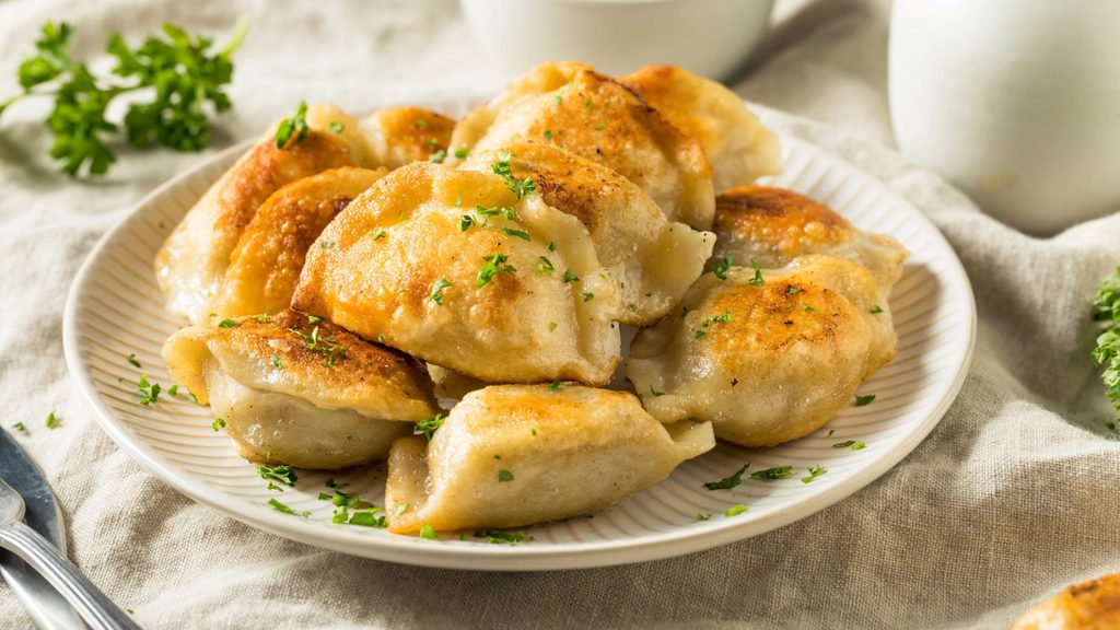 A plate of pan-fried dumplings garnished with chopped parsley for National Pierogi Day.