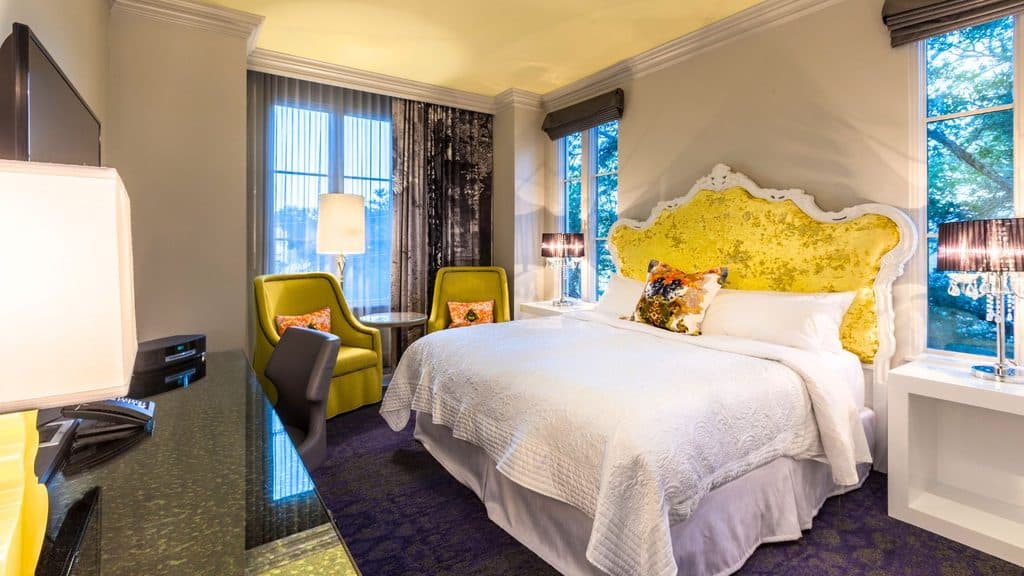 Hotel room with a king bed featuring a bright yellow headboard, two green armchairs, and a desk.