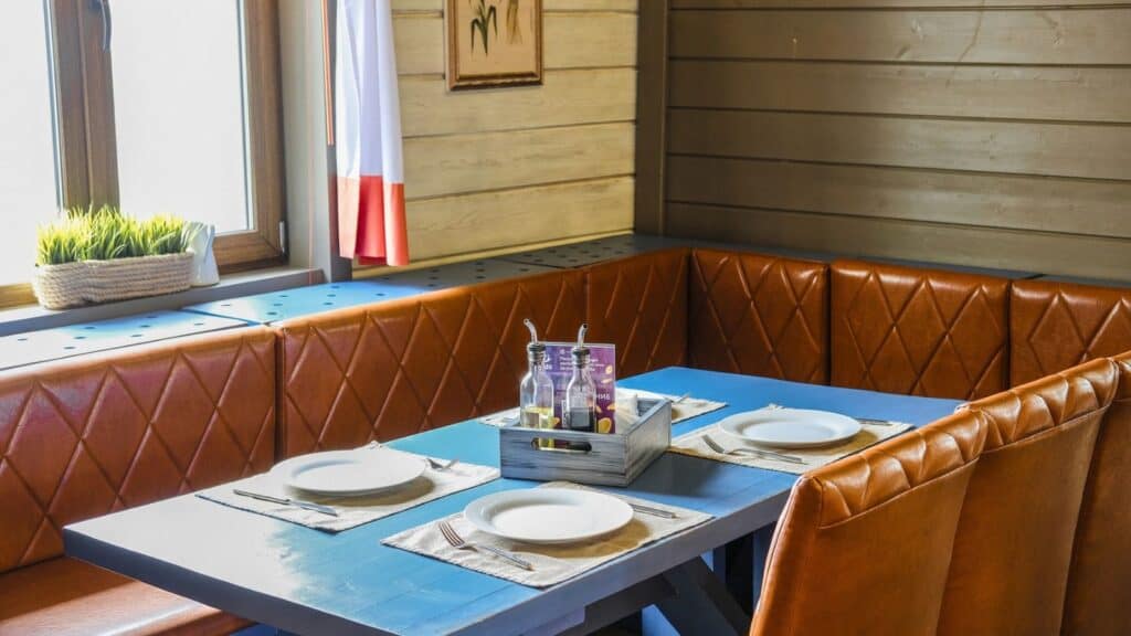 Blue wooden dining table with place settings and a central condiment caddy, surrounded by brown tufted leather booth seating.