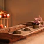A massage table prepared with towels, three smooth stones, and a lily, with candles in the background.