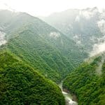 A river flows through a deep, mist-covered mountain valley forested with green trees.
