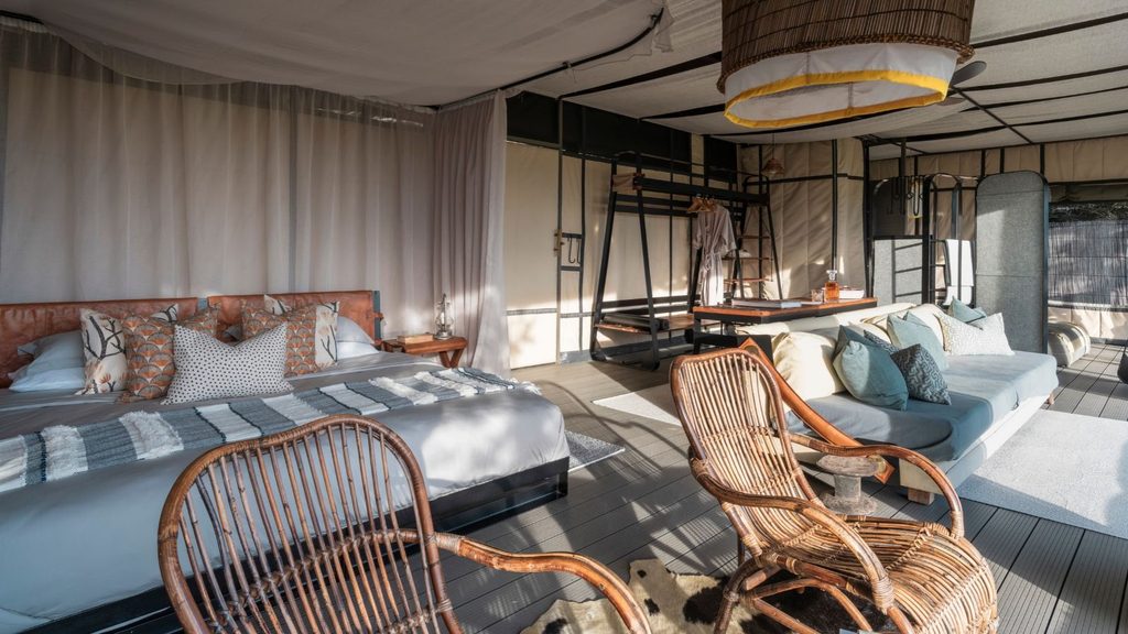 Interior of a luxury tent in Liuwa Plain National Park, featuring a bed, a sofa, two rattan chairs, and a metal storage frame.