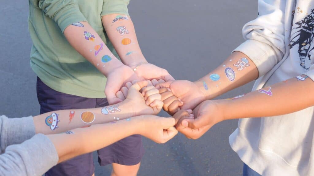 Four children&rsquo;s arms held together in a circle, each wearing space-themed temporary tattoos that kids loved.