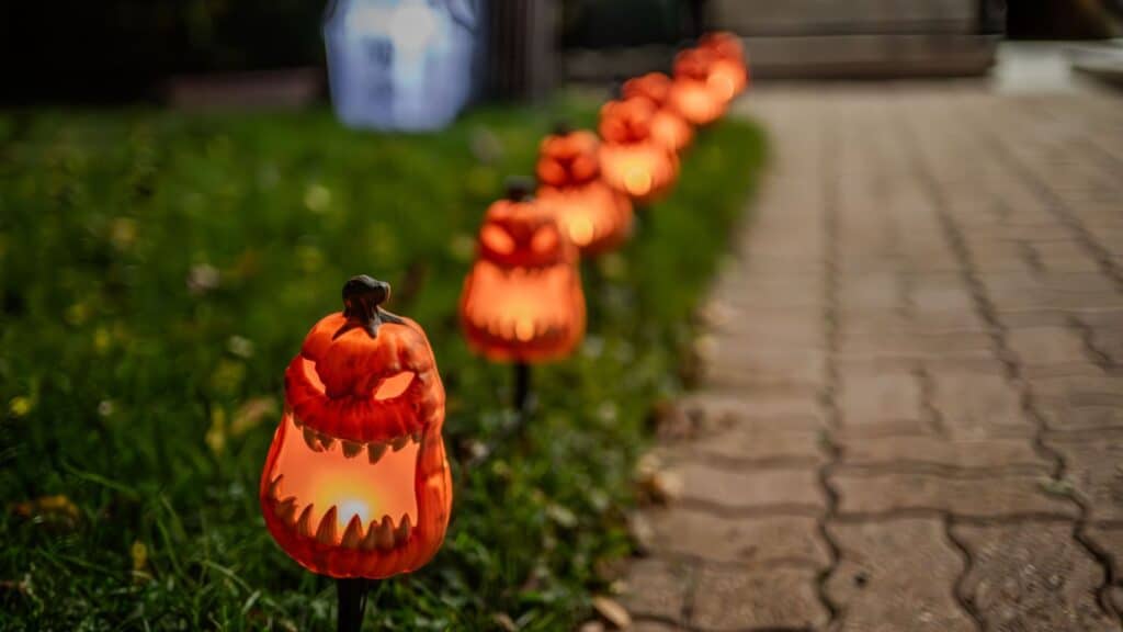 A row of glowing, orange jack-o&rsquo;-lantern pathway lights lining a walkway in compliance with HOA Halloween rules.