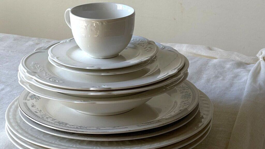 A teacup sitting atop a stack of white porcelain plates and bowls from a gas station promotion.